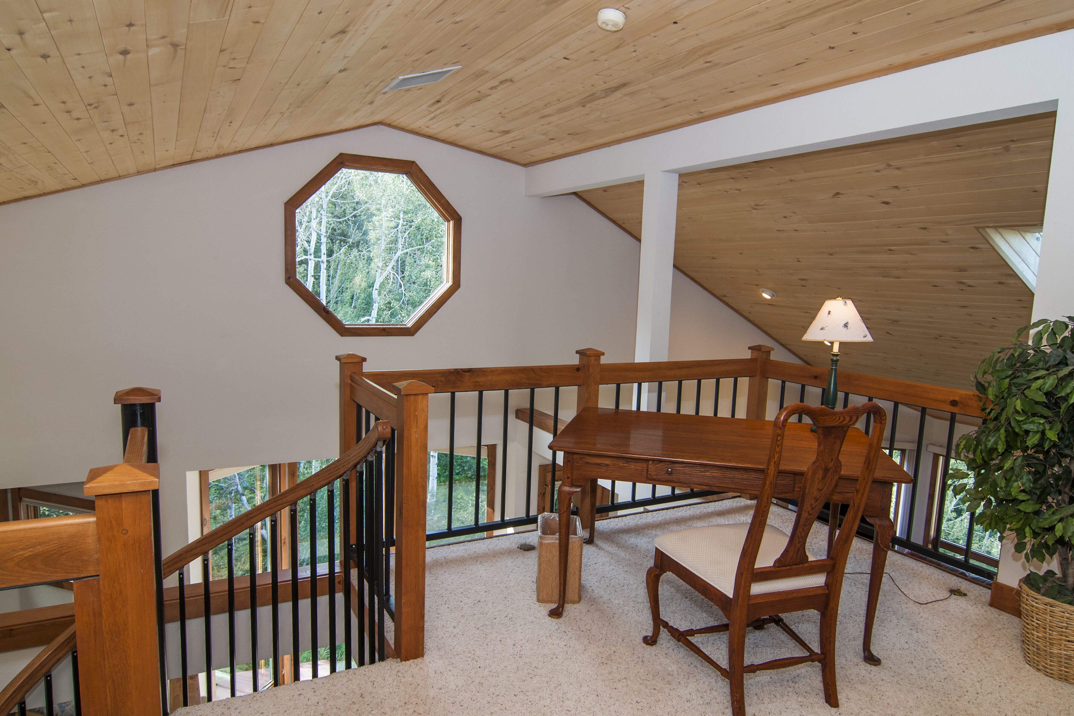 A wooden staircase with a railing, a dining table with chairs, and a potted plant.