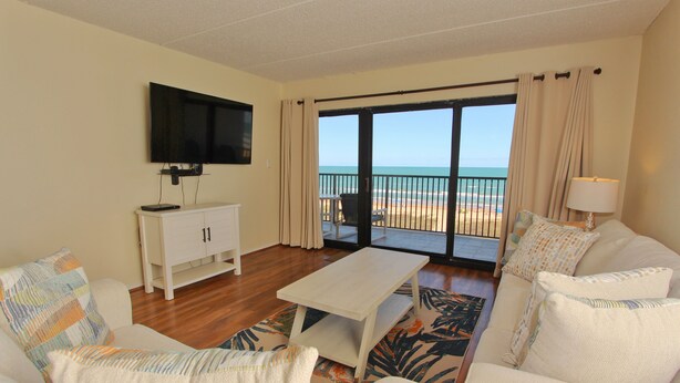 A living room with a flat-screen TV, a white sofa, a coffee table, and a view of the beach through a sliding glass door. - Oceanside Zen Escape - Condo 503: 2BR, 2BA retreat in South Padre Island. (South Padre Island)