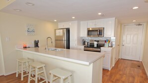 A kitchen with a central island, white cabinets, stainless steel appliances, and wooden stools. - Oceanside Zen Escape - Condo 503: 2BR, 2BA retreat in South Padre Island. (South Padre Island)