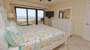 Un dormitorio con cama, cómoda, televisor y balcón con vistas a la playa.