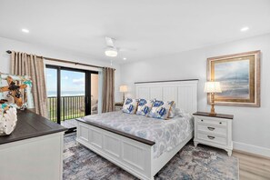 Un dormitorio con cama, mesitas de noche, lámpara de noche, ventilador de techo, ventana con cortinas y vistas al exterior.