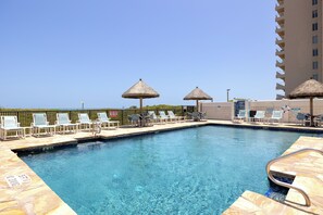 A pool area with lounge chairs and umbrellas, a clear sky, and a building in the background.