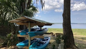 Un área techada para el almacenamiento de embarcaciones con tres kayaks, un muelle de madera y vista a un lago.