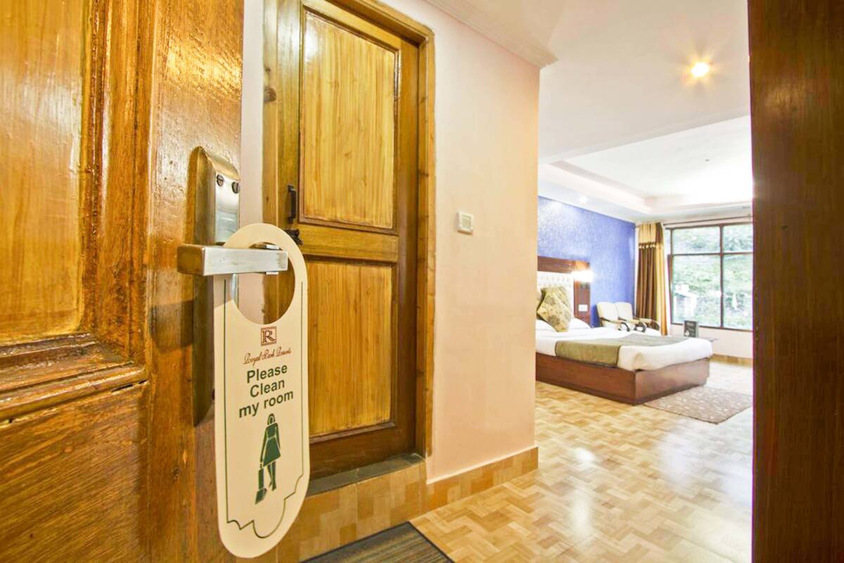 Ein Hotelzimmer mit einer Holztür, einem Bett mit blauem Kopfteil und einem Fenster mit Vorhängen.