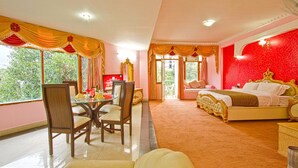A hotel room with a dining area, a large bed with ornate headboard, and a view of greenery outside. - Royal Park Resort (Manali)