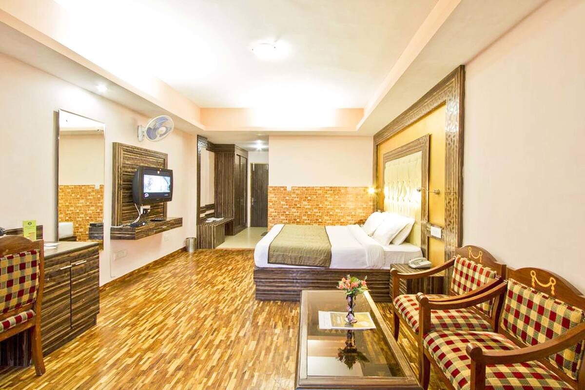 Ein Hotelzimmer mit Holzboden, einem Bett, einem Sofa, einem Couchtisch, einem Fernseher und einem durchgehenden Türspalt sichtbaren Badezimmer.