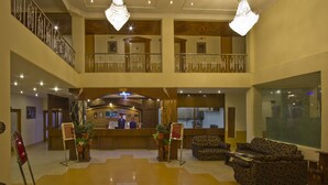 A hotel lobby with a reception desk, seating area, and a second-floor balcony. - Royal Park Resort (Manali)