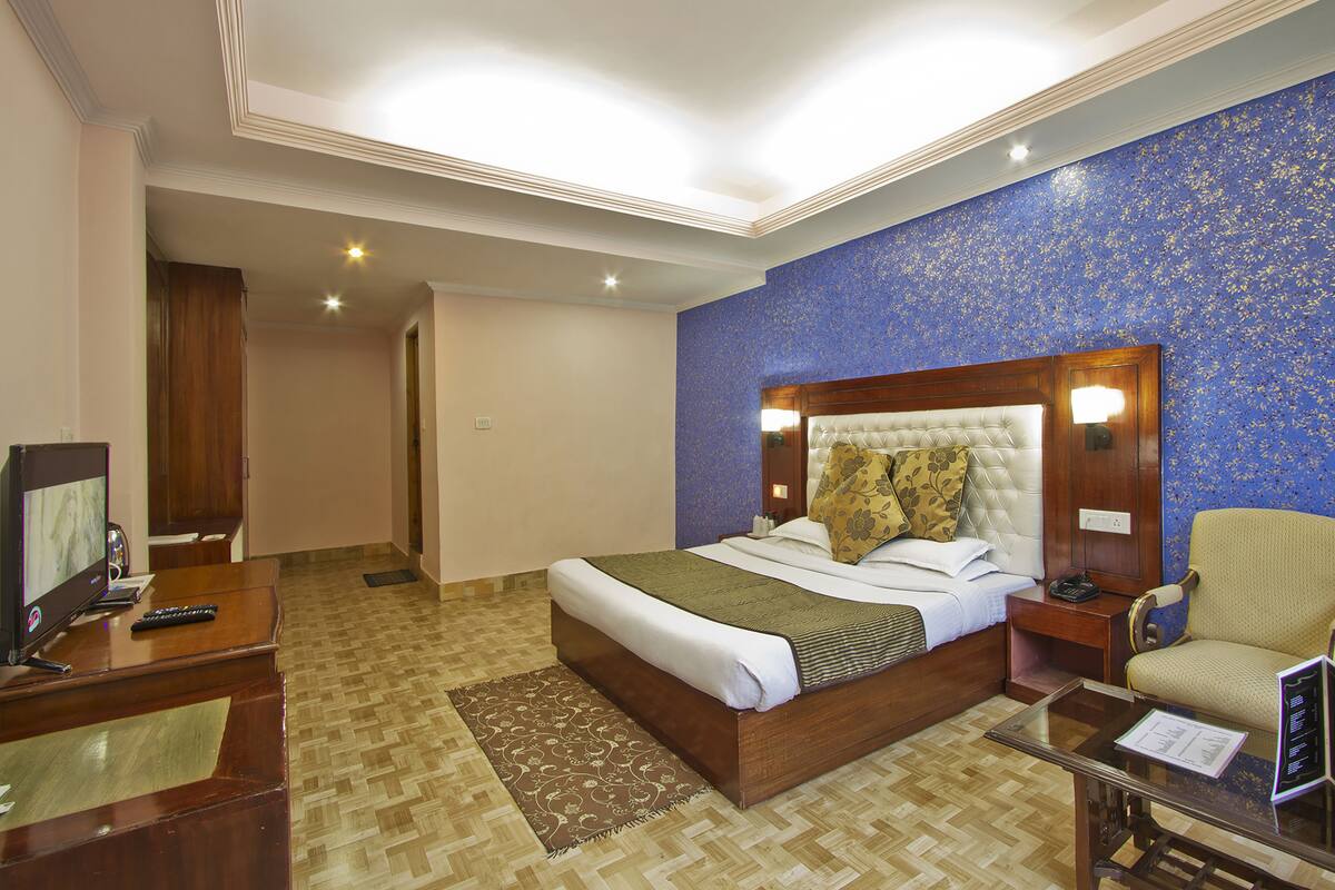 Ein Hotelzimmer mit einem großen Bett, einem Schreibtisch mit Computer, einem Sessel und einem Fernseher.
