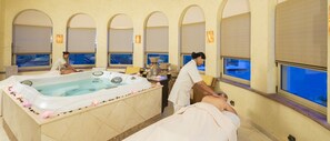 Et spa-område med et stort jacuzzi, to massageborde og en dekorativ vase.