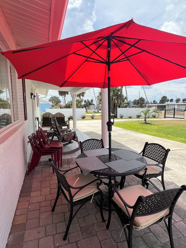 An outdoor patio with a red umbrella, black metal chairs, and a table.