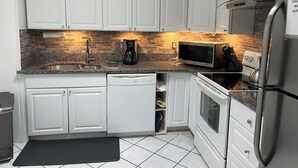 A modern kitchen with white cabinets, a granite countertop, a stainless steel refrigerator, a microwave, a coffee maker, and a gas stove. - Beautiful vacation home - just 2-Minute Walk to World-Famous Daytona Beach (Daytona Beach)