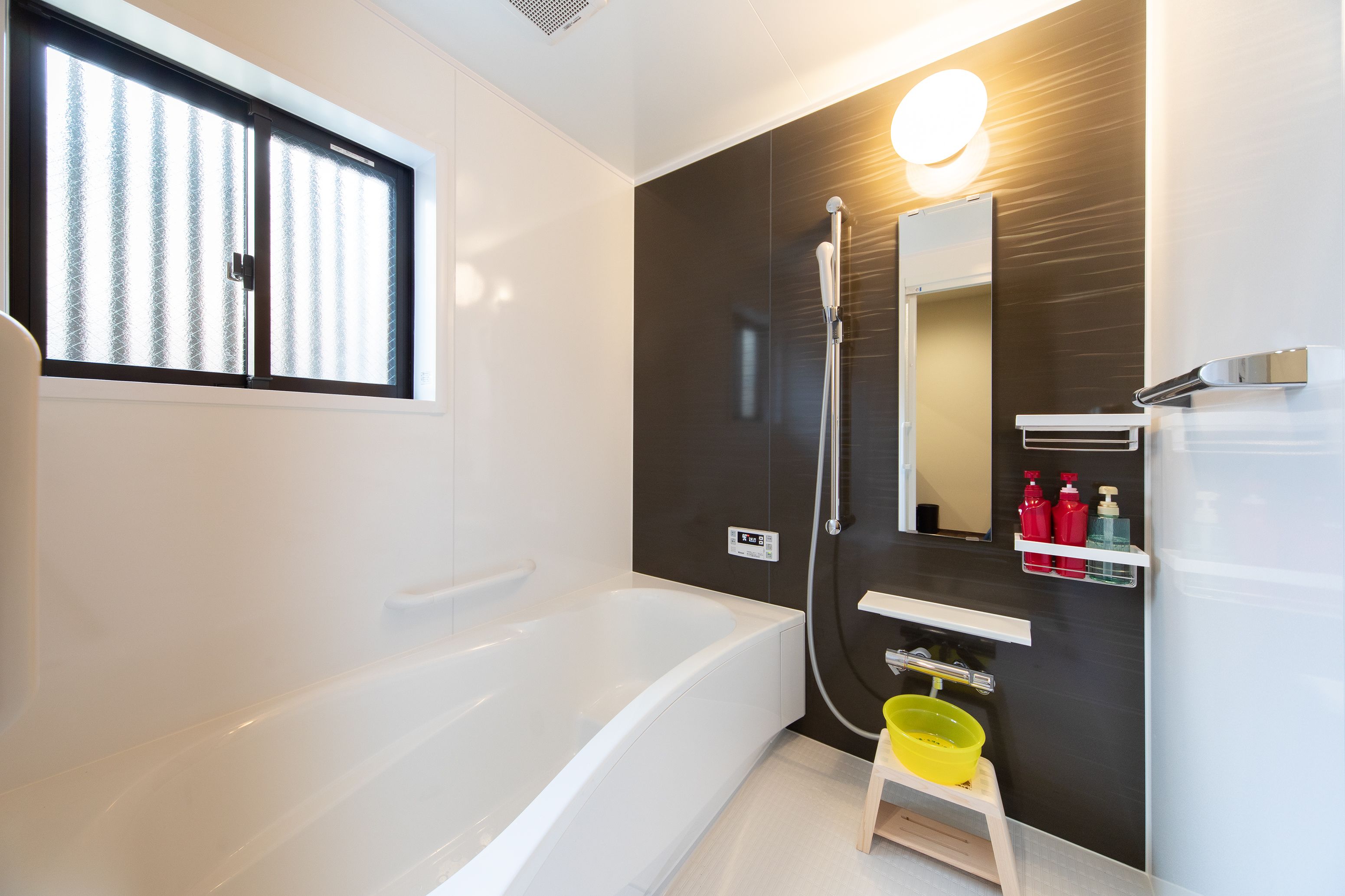 A modern bathroom with a bathtub, a shower, a mirror, and a shelf with toiletries.