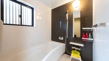 A modern bathroom with a bathtub, a shower, a mirror, and a shelf with toiletries.