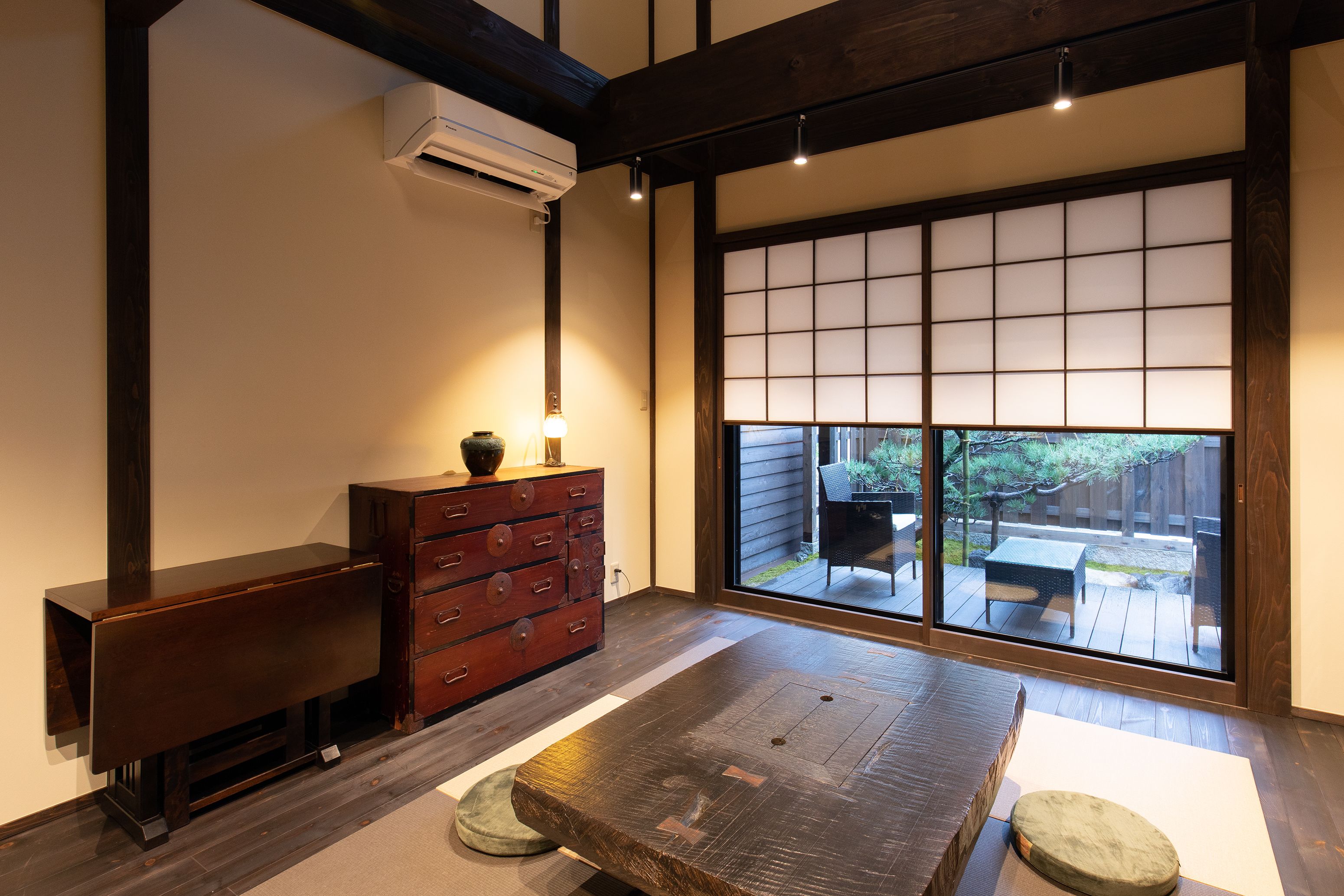 A traditional Japanese room with tatami flooring, a low wooden table, a red chest of drawers, and a sliding glass door leading to an outdoor patio.