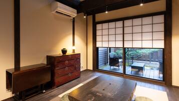 A traditional Japanese room with tatami flooring, a low wooden table, a red chest of drawers, and a sliding glass door leading to an outdoor patio.