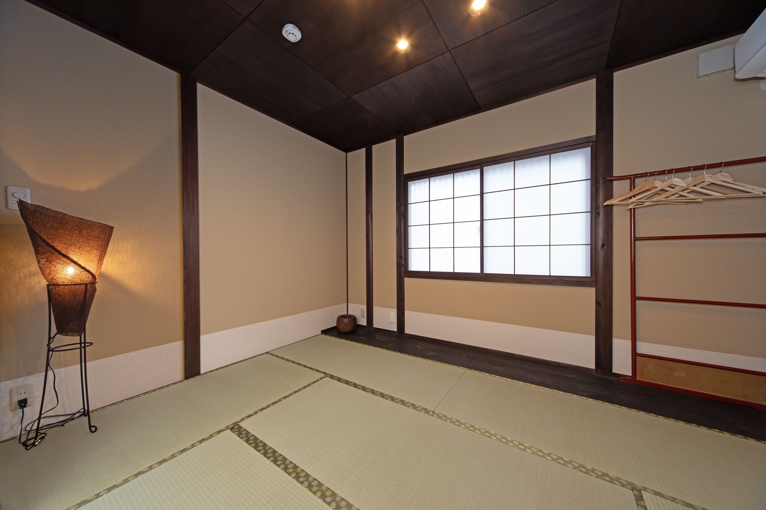 Una habitación japonesa tradicional con suelo de tatami, ventana con pantalla shoji y un perchero.