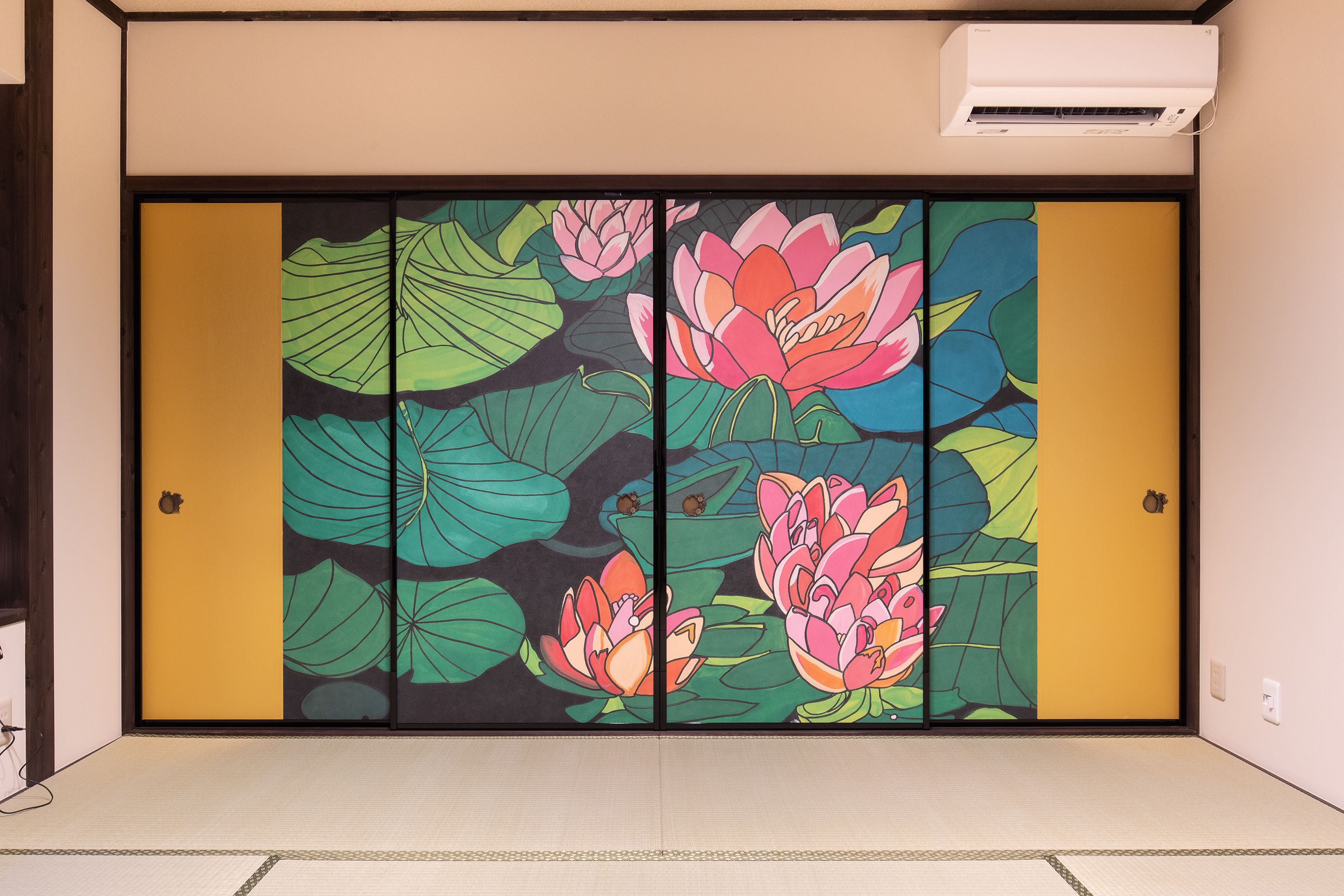 A room with a sliding door featuring a vibrant floral design, a small air conditioning unit above it, and a tatami mat floor.
