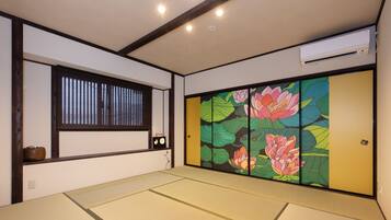 Habitació japonesa tradicional amb sòls de tatami, una porta corredissa amb decoració floral, una finestra amb persianes i un aparell d'aire condicionat.
