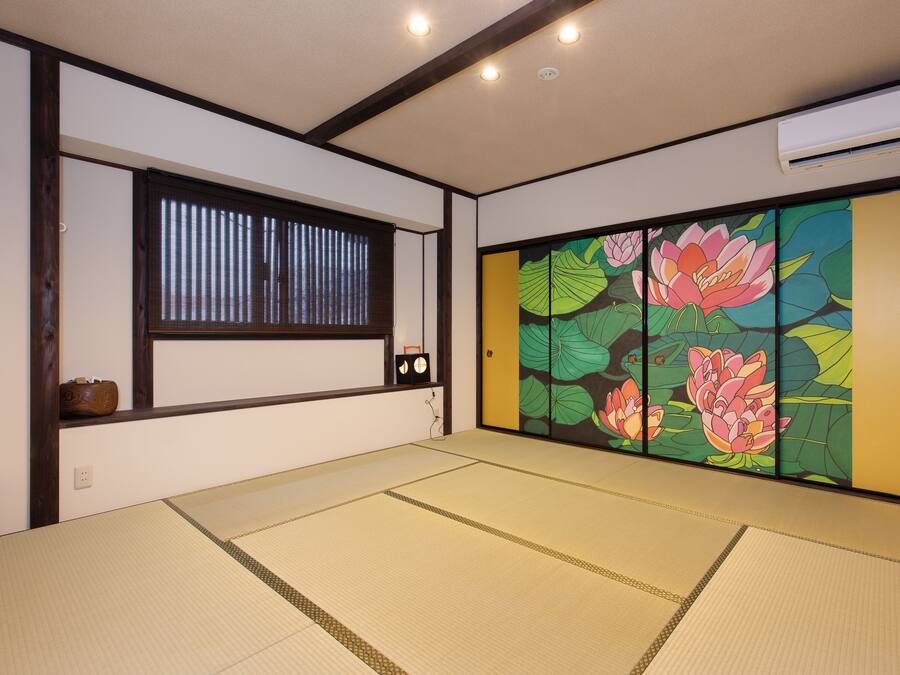 Habitació japonesa tradicional amb sòls de tatami, una porta corredissa amb decoració floral, una finestra amb persianes i un aparell d'aire condicionat.