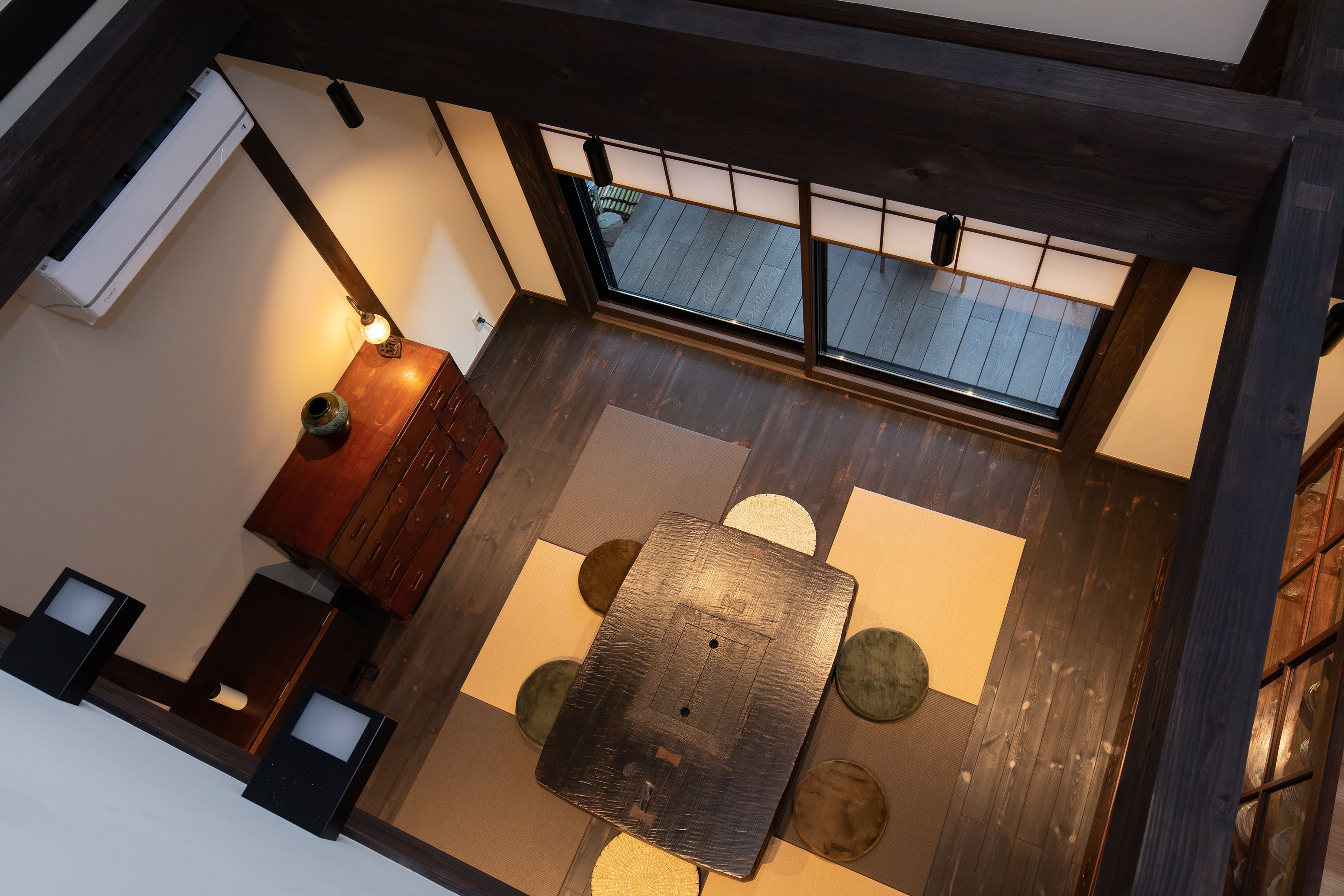 A room with a wooden floor, a central table, and a view through a window.