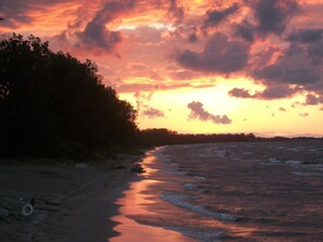 Ein Strand mit Sonnenuntergang, Wellen und einem bewaldeten Gebiet.