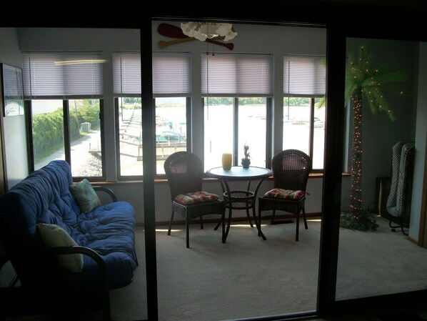 A room with a blue sofa, two wicker chairs, a small round table, and a view of a pool area through large windows.