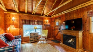 L’intérieur d’un chalet chaleureux, avec un canapé à carreaux, un petit fauteuil, une cheminée et un téléviseur.