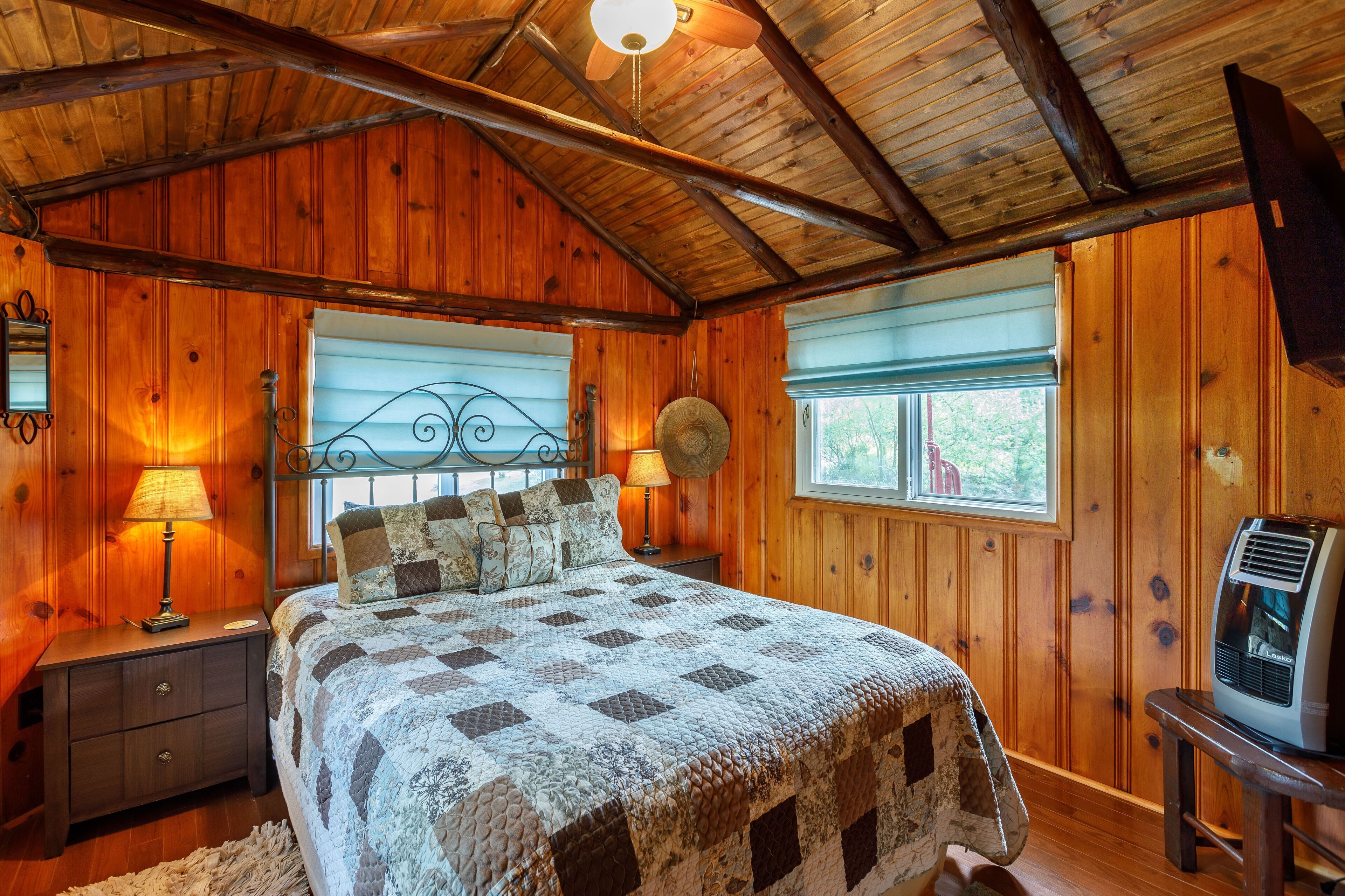 A wooden cabin bedroom with a bed, two bedside lamps, a heater, and a television on a wooden stand.