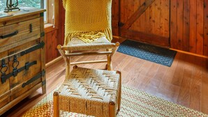 L’intérieur d’un chalet en bois, avec une chaise en osier, une commode en bois et une fenêtre donnant sur les arbres.
