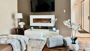 Een moderne woonkamer met een flatscreen televisie aan de muur, een witte salontafel, een bank en een houten vloer.