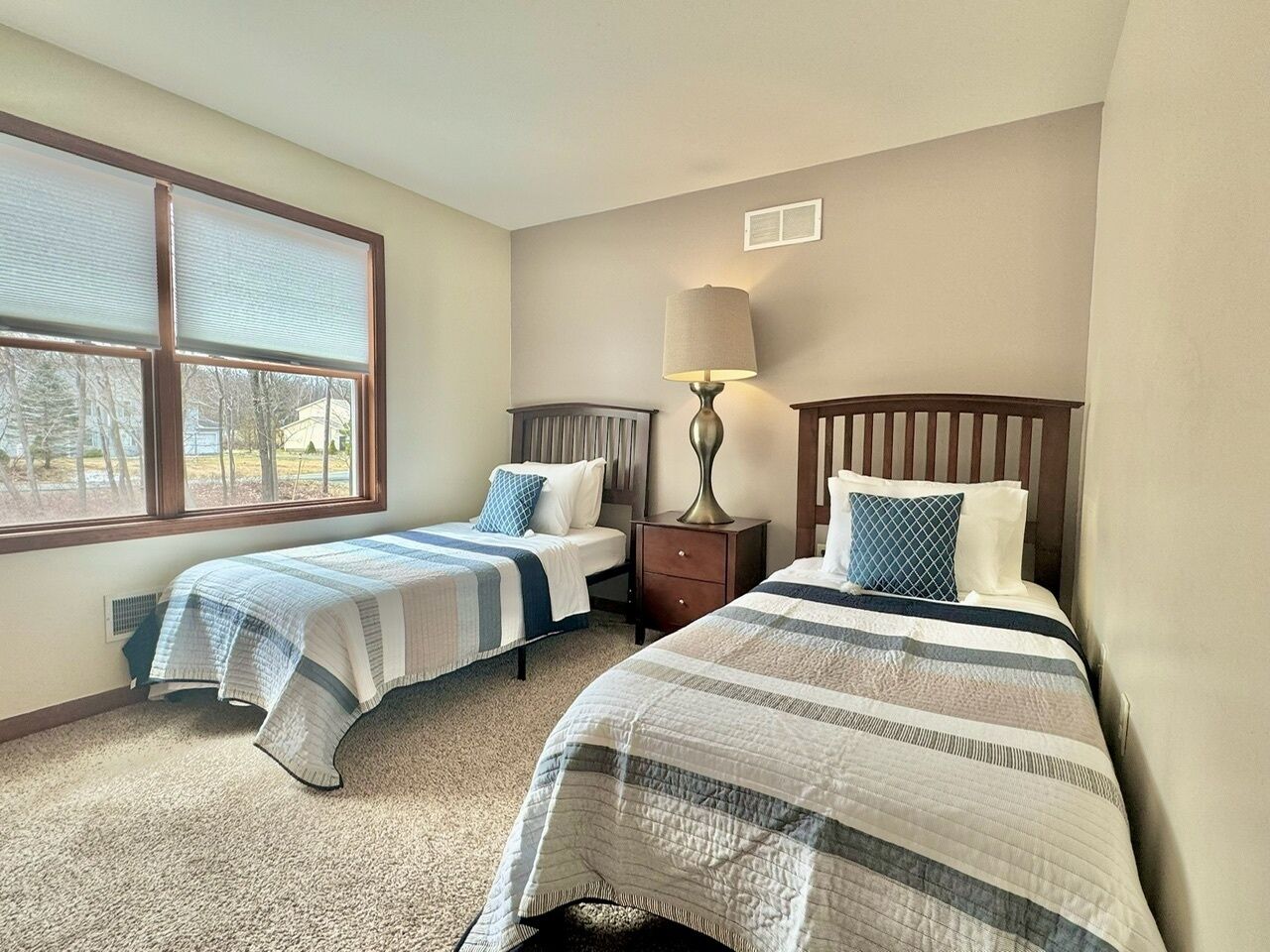 A bedroom with two beds, a nightstand, a lamp, and a window with blinds.