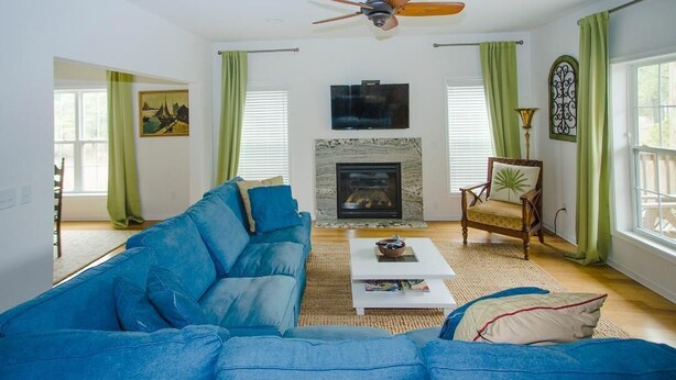 Ein Wohnzimmer mit blauem Sofa, Kamin, Deckenventilator und Fernseher über dem Kamin.