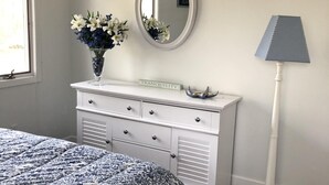 Une chambre à coucher avec un lit, une commode, un miroir, un vase de fleurs et une lampe.