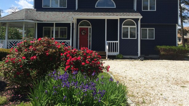 Une maison à deux étages, avec une façade bleu foncé, une porte d’entrée rouge et un porche abrité.