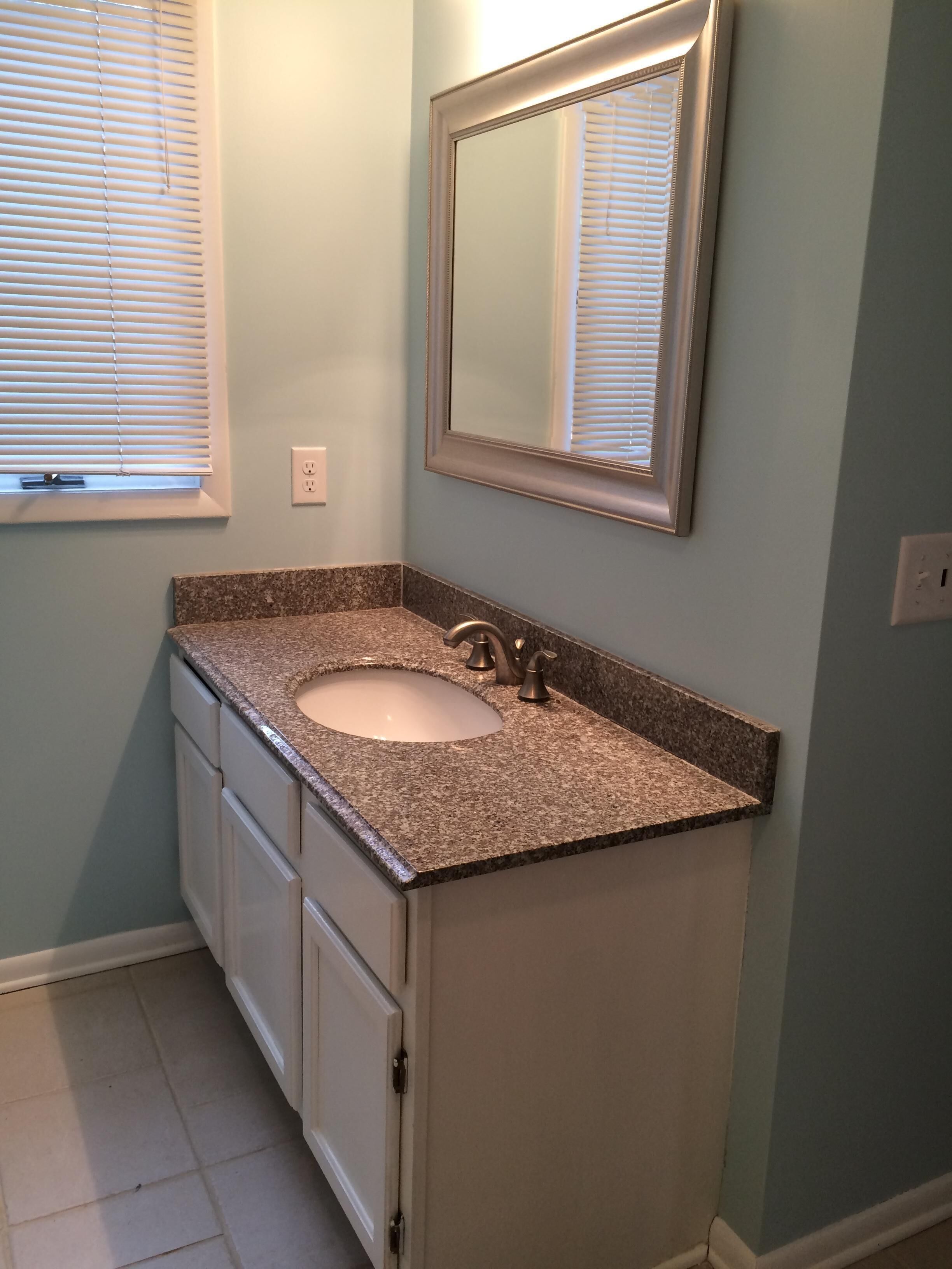 A bathroom with a granite countertop sink, a mirror, and white cabinetry.
