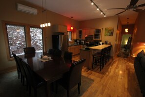 A modern kitchen with wooden cabinets, a stainless steel refrigerator, and a dining area with a wooden table and chairs.