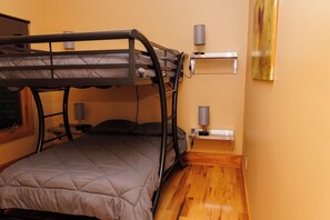 A bunk bed with a headboard, a bedside table, two lamps, and a wooden floor.