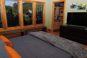 Un dormitorio con cama, cómoda, televisor y ventana con vista a árboles.