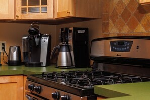 A kitchen with a gas stove, a coffee maker, and a coffee machine.