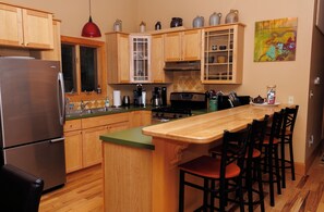 Una cocina con gabinetes de madera, un refrigerador de acero inoxidable, una cafetera y un comedor con sillas.