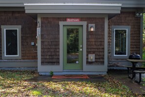 A building with a green door and a sign above it that reads 'Red Hawk.' There are two windows on either side of the door, and a small outdoor table is visible to the right.