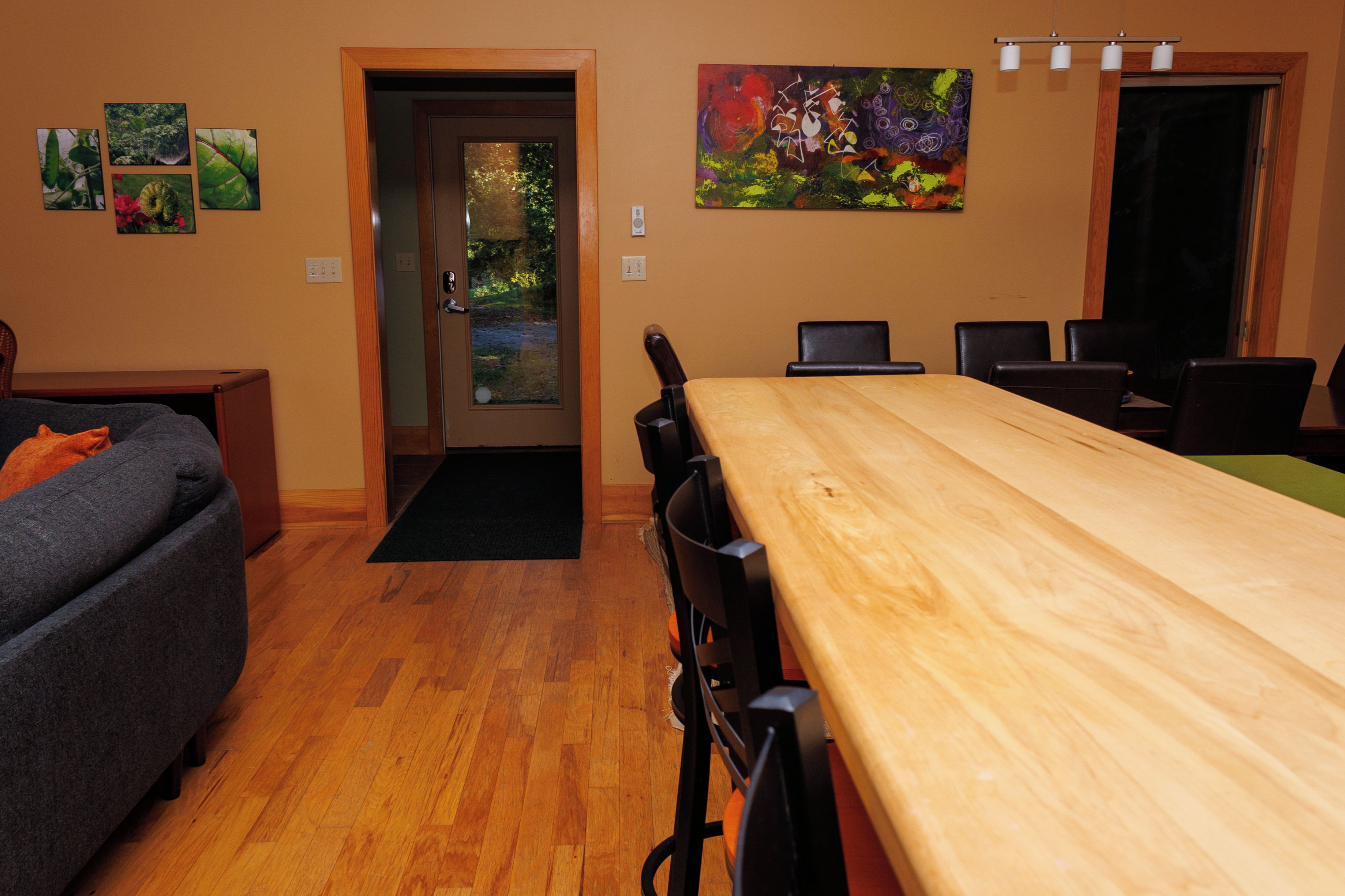 A room with a wooden dining table, black chairs, a grey sofa, and a door leading to a garden.