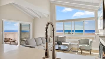 A modern living room with a view of the beach, a large window, and a unique kitchen faucet.