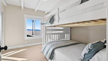 A bunk bed room with a window overlooking a beach, a ceiling fan, and a wooden floor.