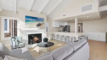 A spacious living room with a fireplace, a large sofa, and a dining area with bar stools.