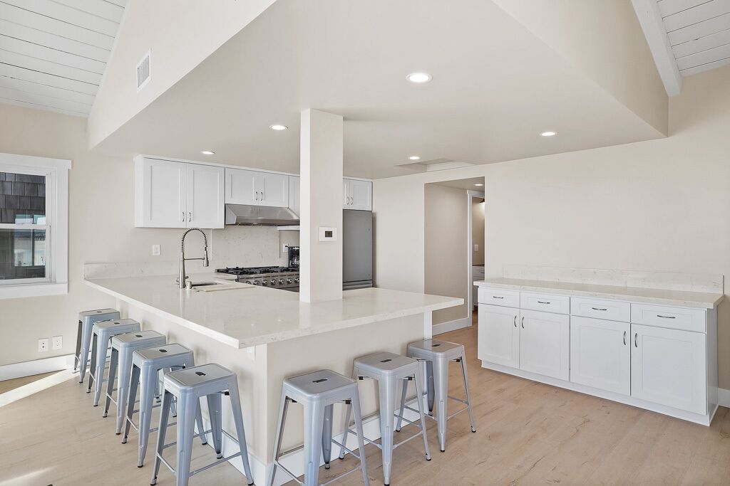 A modern kitchen with white cabinetry, a central island with stools, and a large window.