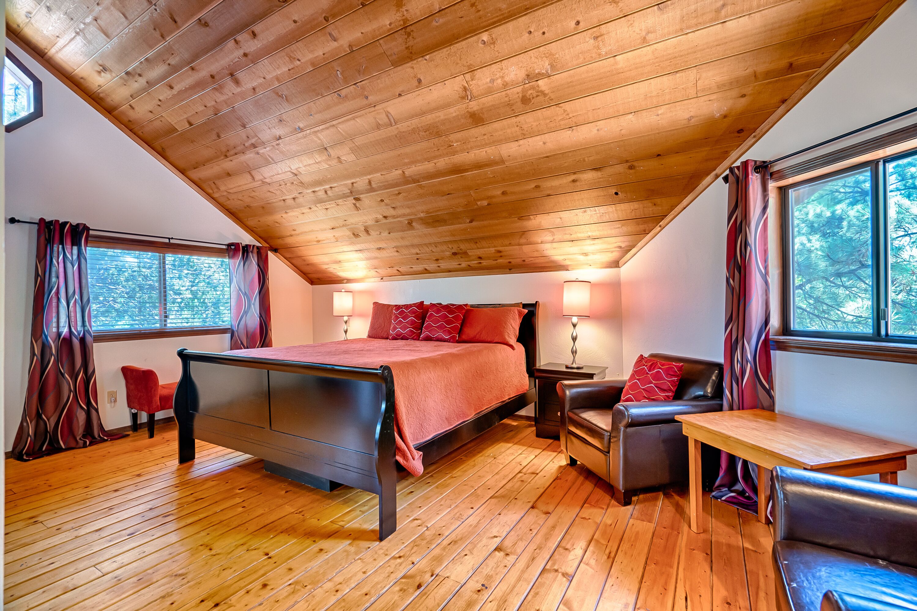 Une chambre avec un plafond en bois, un lit, un bureau, deux chaises et une fenêtre avec des rideaux.
