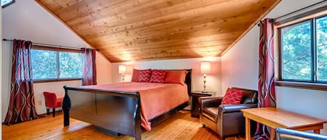 Une chambre avec un plafond en bois, un lit, un bureau, deux chaises et une fenêtre avec des rideaux.
