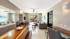 A spacious living area with a wooden dining table, grey sofas, and a ceiling fan.