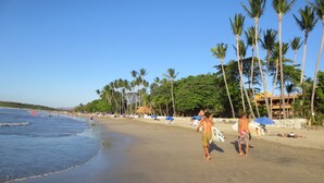 A beach with palm trees, umbrellas, and people.